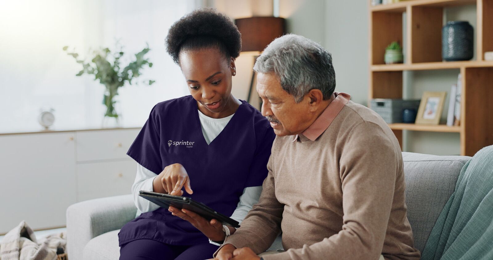 A Sprinter clinician reviewing care information on a tablet with a senior patient at home