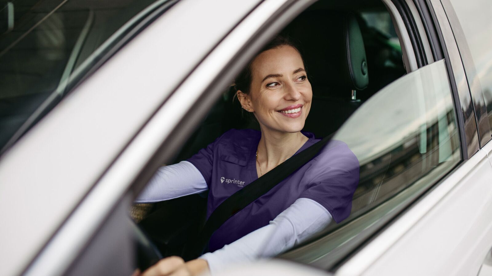 A Sprinter Health clinician smiling from the driver's seat of her car