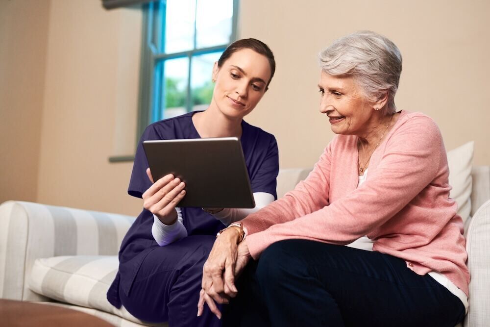 A Sprinter Health clinician reviewing care information on a tablet with a senior patient at home